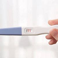 Dámské ruce držící pozitivní těhotenský test s jemným srdíčkovým pozadím